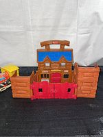 Front view of the Fisher Price Western Fort playset showing overall structure, blue roof, red gates, and log cabin style walls.