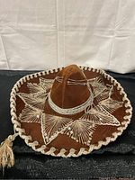 Full view of brown velvet Mexican sombrero showing white embroidery and white braided trim on brim.