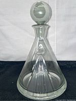 Full view of the glass decanter with the round stopper on a black surface with white background.
