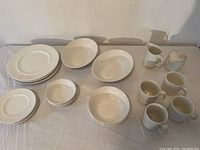 Full set of Athena white ironstone dinnerware including four place settings with plates, bowls, and cups, plus two serving bowls, cream pitcher, and sugar bowl with lid displayed on a table.