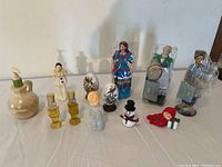 Photo showing multiple ceramic figurines and Avon perfume/cologne bottles arranged on a table against a beige background