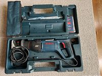 Open carrying case showing Bosch electric reciprocating saw with power cord and several saw blades inside case compartments