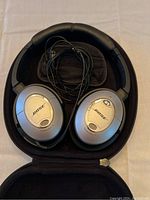 Bose QuietComfort 15 headphones inside black zippered hard case, silver ear cups with Bose logos and wired cable visible.