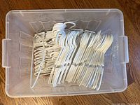 Plastic child-sized white hangers packed in a large clear plastic bin, stacked and organized neatly, showing quantity and condition.