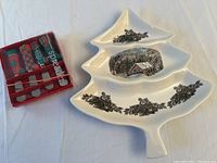 Ceramic Christmas tree-shaped serving dish with winter village and decorative holly motifs next to boxed red and green holiday spreaders.