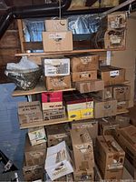 Photo showing multiple cardboard boxes stacked on wooden shelving with labels like 'mugs mostly Sheldon,' 'blue pottery,' 'china pieces,' and others indicating the contents inside.