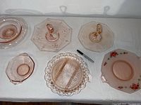Top view of all 10 Depression Glass pieces on white cloth, showing pink and white items, mixed shapes and patterns.