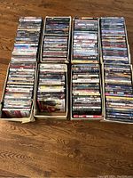 Top-down photo showing eight boxes filled with DVD movies arranged in two rows of four on a wood floor.