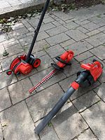 Three Black & Decker outdoor electric garden tools on a stone patio: the edging machine with wheels, hedge trimmer with prominent blade, and leaf blower with nozzle.