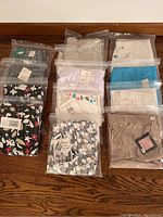 Multiple pairs of women's capri pants, folded and sealed in clear plastic bags. Includes solid colors like beige, white, blue, and multiple floral and printed designs visible.