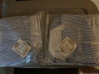 Two blue and white vertically striped pant and top sets packaged in clear plastic bags with a white base top showing a blue stripe border and a tag.