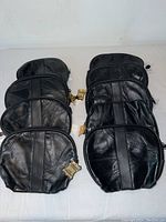 9 black leather clutch purses stacked together showing consistent size, color, and zipper detail