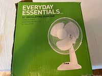 Green box labeled Everyday Essentials containing a 12" oscillating desk fan with key features marked on front: 3-speed settings, adjustable vertical tilt, 90° oscillation.