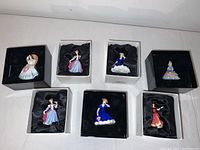 Seven miniature ladies figurines displayed inside their black and white boxes with satin lining, showing their detailed colorful dresses.