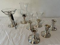 Six sterling silver candle holders on white cloth: compote, hurricane lamps and squat candlesticks with a marker for scale