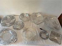 Overview of eight vintage glass bowls and serving trays with sterling silver overlay decoration arranged on a surface wrapped in protective plastic.