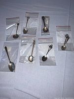 Photo showing seven sterling silver spoons each individually bagged, displaying various ornate handle designs and sizes.