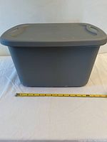 Single grey Rubbermaid storage box with lid on, placed on white surface with measuring tape showing approximately 13 inches width.