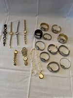 Grouping of all 18 ladies costume watches showing different styles and bands on white cloth background.