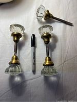 Top down view of 4 of the 5 glass and brass door knobs showing brass fixtures and threaded rods along with a marker for size comparison.