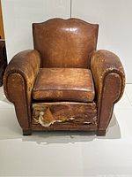 Front view of tan leather armchair showing wear on seat cushion and torn front skirt