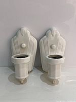 Pair of white glazed Art Deco porcelain wall sconces showing front view with bulb sockets and decorative switch knobs.