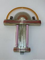 Full front view of sconce showing chrome backplate, amber glass ring, red accent stripes, pink glass tubes and central disc
