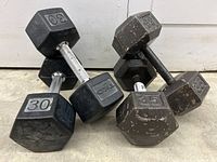 Photo showing two 30lb rubber hex dumbbells with chrome grip alongside two 35lb steel hex dumbbells with visible wear and surface rust.