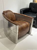 Three-quarter front view of chair showing curved aluminum exterior panels and leather upholstery.
