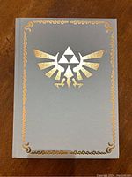 Front cover of the hardcover book showing gray cover with gold embossed Triforce and Hylian Crest symbols.