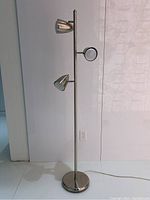 Full view of the standing lamp showing metal pole with three adjustable light heads and round base on floor.