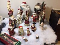 Wide view showing the Santa figurines in a wintery setup on white cotton resembling snow, arranged in several rows including larger standing Santas and smaller collectible pieces