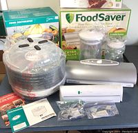 Full view of FoodSaver vacuum sealer, Deni food dehydrator, original boxes, vacuum seal bags, and accessories packed in plastic bags