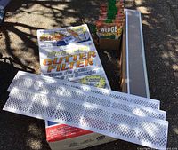 Photo showing white plastic snap-in gutter filters laid over a box labeled 'Snap-In Gutter Filter' and a long metal mesh gutter filter, along with a box holding downspout screens.