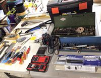 Various hand tools including screwdrivers, pliers, hammer drill and bits, socket set, and tool parts laid out on table