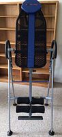 Full front view of the inversion table showing mesh backrest, padded blue headrest, silver metal frame, foot and ankle supports.
