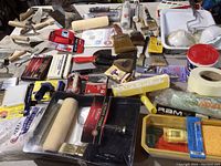 Full overview of assorted painting, tiling, and concrete finishing tools and supplies spread on a surface