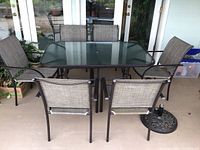 Front view of patio table with six chairs arranged around it, showing the clear tempered glass surface and metal mesh chair seats
