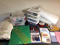 Full lot overview showing cutting mat, ruler, sewing books, fabric roll, storage bins with sewing notions and fabric, tin of buttons