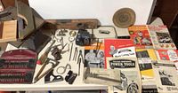 Wide view of many vintage tools on a white table with tool manuals and magazines arranged on the right side.