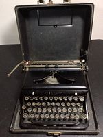Open view of portable black typewriter inside its case showing keyboard and carriage return lever