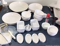 Full collection of white ceramic and Corelle serving dishes including Corningware soup bowls with rubber lids, loaf pans, crème brûlée dishes, bowls, quiche platter, salad bowl, and butane torch with fuel canister.