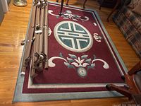 Full view of oriental area rug on hardwood floor with some folded metal stand pieces on top of rug.