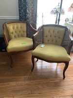 Pair of vintage French style arm chairs with caned backs and yellow upholstered seats and tufted backs, wooden frames with carved curved legs sitting on hardwood floor.