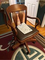 Wood swivel office chair by Bassett brand with leather seat showing the entire chair and paper with warranty info placed on the seat.