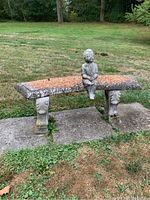 Full view of outdoor cement bench with child statuette sitting in middle, showing location and condition.