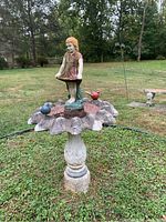 Full view of cement birdbath in outdoor setting, showing central girl statuette and bird figurines on scalloped edge basin.