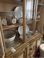 White Huntington china set with plates, cups, and saucers on display cabinet shelves along with glassware and other items.