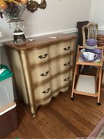 Photo of vintage French Provincial style dresser showing full front view. Features three drawers with ornate metal pull handles, scalloped shaped drawer fronts, and wooden curved top.