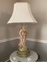Front view of ceramic figural female lamp on a small round table with white fabric lampshade.